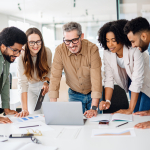 Five adults stand around a laptop on a table