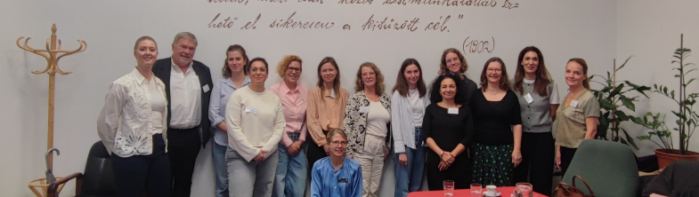 A group of people stand in front of a white wall with text written on it in Hungarian