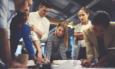 A group of people standing around a table, writing on charts