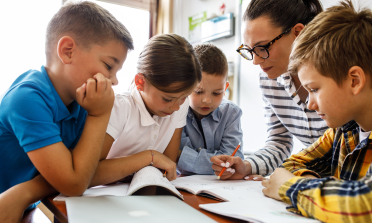 Four children and their teacher look at a workbook together