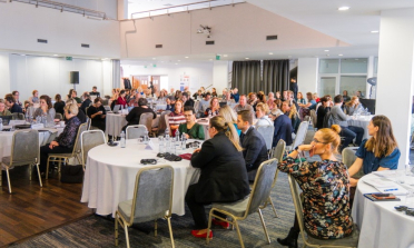 Groups of people sit around tables in a conference room